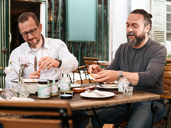 REWE Kaufmann Andre Becker und Lokal-Partner Robert Buljat essen gemeinsam Aioli mit Brot. 