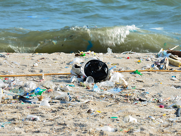 Eine Welle spült Plastikmüll an einen von Plastikabfällen übersäten Strand 