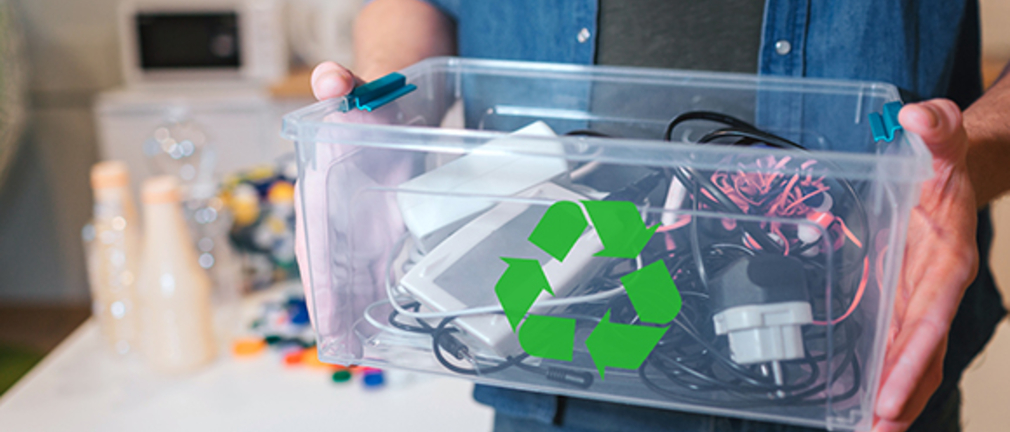 Ein Mann hält eine Kiste mit alten Elektrogeräten und Kabeln 