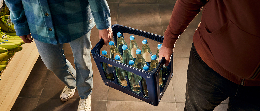 Zwei Männer tragen eine Wasserkiste mit Glasflaschen 