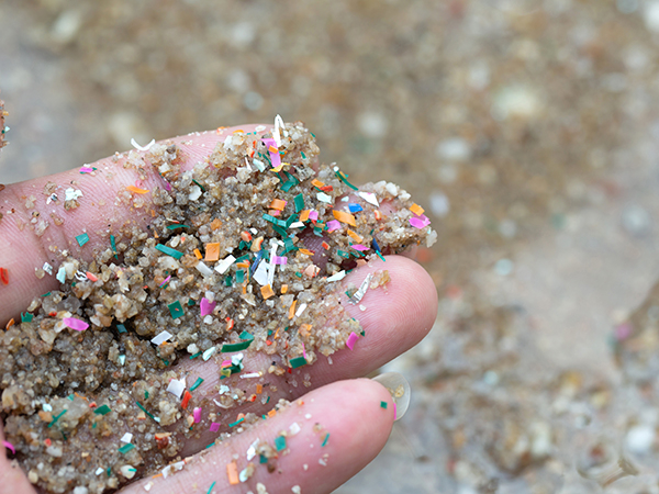 Sand und bunte Mikroplastik-Teilchen in einer offenen Hand 