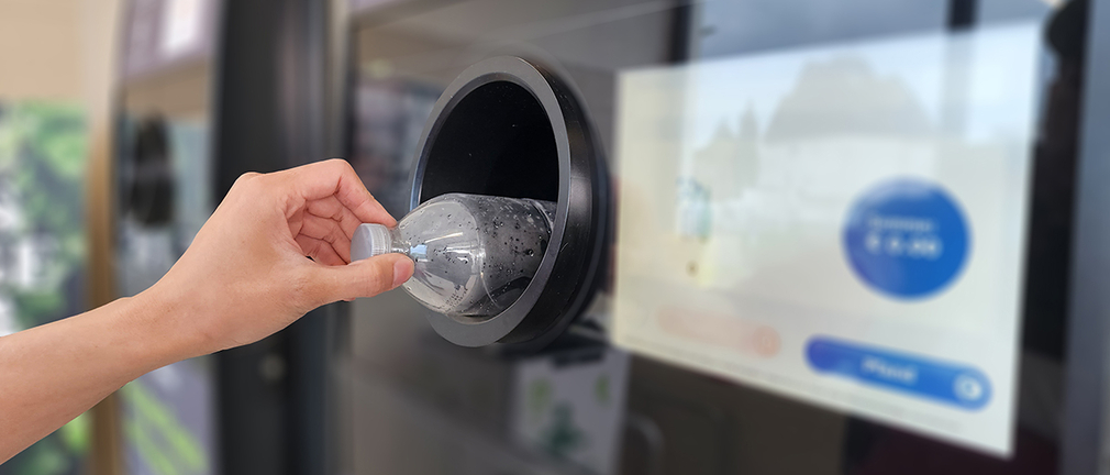 Eine Hand legt eine Plastikflasche in einen Pfandautomaten