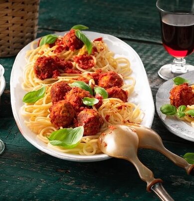 Auf einem gedeckten Tisch stehen zwei Teller und eine Servierplatte voll Spaghetti mit Linsenbällchen. 