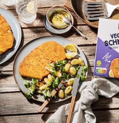 Mehrere Teller mit knusprigen veganen Schnitzeln und Gnocchi-Salat. 