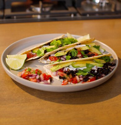 Ein Teller Tacos – gefüllt mit schwarzen Bohnen, Tomaten, roten Zwiebeln, Avocado und frischen Kräutern. 