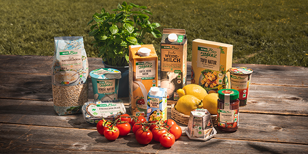 Verschiedene REWE Bio und REWE Bio + vegan Produkte stehen draußen auf einem Holztisch.