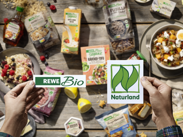 Hände halten REWE Bio und Naturland Logo, im Hintergrund verschiedene REWE Bio Produkte