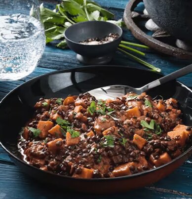 Zwei Teller mit veganem Belugalinsen-Curry stehen neben dem leeren Topf auf einem Tisch. 