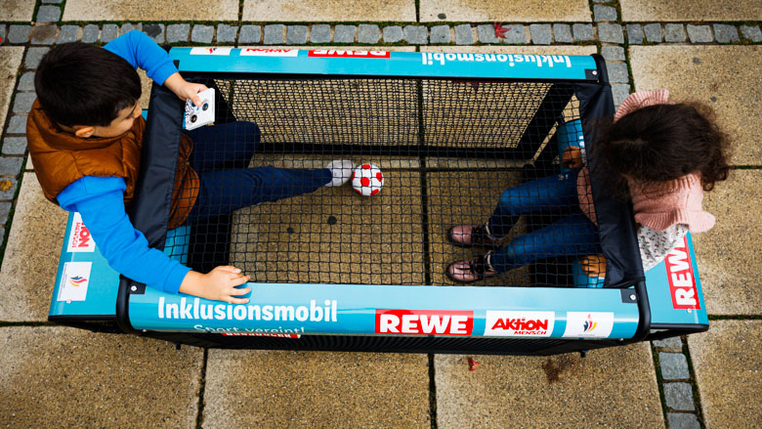 Zwei Kinder spielen Fußball an einem inklusiven Sportgerät.