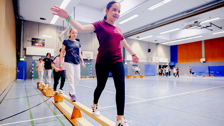 Mehrere Jugendliche mit und ohne Behinderung balancieren auf umgedrehten Sportbänken. 