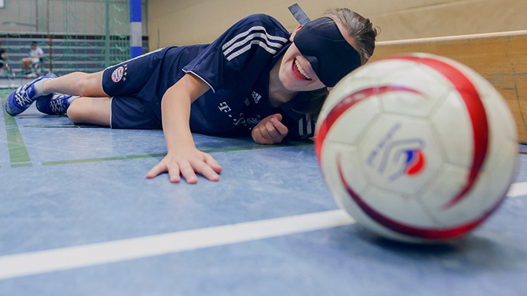 Ein Kind versucht, mit verbundenen Augen einen Handball zu fangen. 
