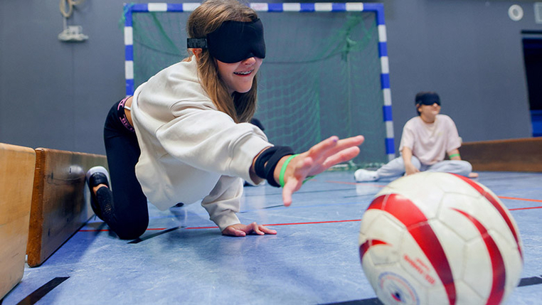 Ein Kind versucht mit verbundenen Augen, einen Ball zu greifen. 