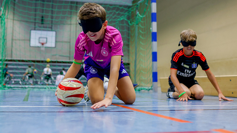 Ein Kind sitzt mit verbundenen Augen im Handballtor.