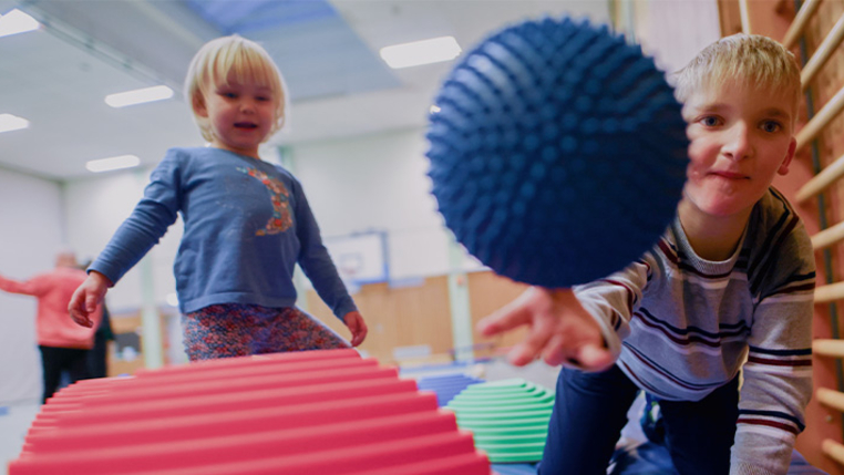 Ein balancieren in einem Geschicklichkeitsparcours. Eines wirft einen Gymnastikball in Richtung Kamera. 