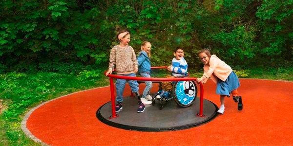 Kinder mit und ohne Behinderung spielen gemeinsam auf einem Universal Karussell mit ebenerdigem Zugang. 