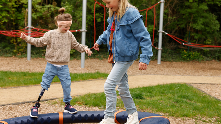Zwei Kinder mit und ohne Behinderung balancieren auf einem inklusiven Spielgerät. 
