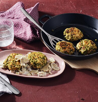 Goldbraune Bratlinge aus Erbsen und Haferflocken auf cremigen Champignons.