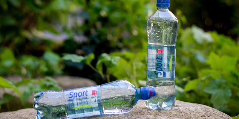 Zwei transparente Plastikflaschen auf einem Stein, im Hintergrund grüne Blätter