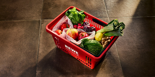 Ein roter REWE Einkaufskorb gefüllt mit unverpackten Produkten. 