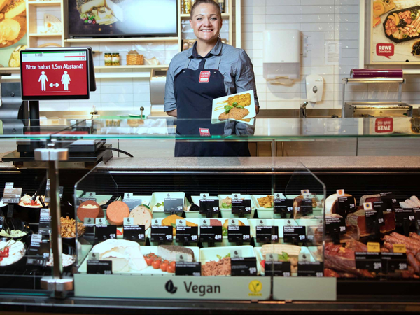 REWE Mitarbeiterin an einer Theke mit veganen Käse-, Wurst- und Fleischalternativen