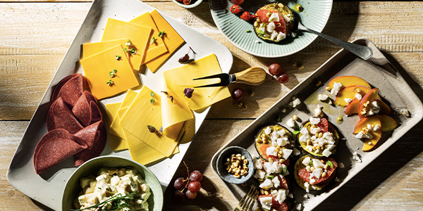 Auf einem gedeckten Tisch steht eine Platte mit pflanzlichem Käse und Aufschnitt. 